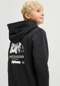 Čierna mikina s kapucňou s grafickým dizajnom na zadnej strane, vrátane horskej imagery a loga v bielej a ružovej farbe. Mäkko jemný materiál.