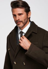 Bruine wollen peacoat met dubbele knopen, geknipte revers en een gestructureerde afwerking, gedragen over een wit shirt en een gestippeld stropdas.