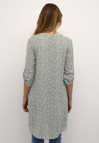 Tunique longue en motif zigzag vert et blanc, avec des manches trois-quarts et un ourlet arrondi, fabriquée en tissu léger.