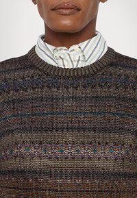 Textured knit sweater in dark brown with horizontal multicolored lines. Ribbed neckline. Light blue and white striped shirt underneath.