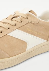 Sáfránybarna nubuk bőr sneaker krémszínű részletekkel, kerek formával, struktúrált felülettel és gumitalppal. Arany logó részletek az oldalon és a nyelvnél.