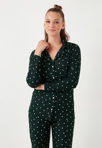 Pijamas verts en tissu doux, avec un motif d'étoiles blanches. La chemise a des boutons et un col ; le pantalon est long et assorti.
