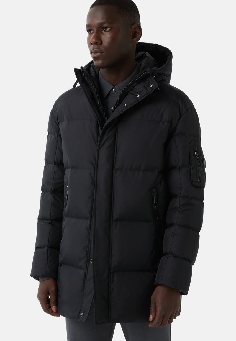 Schwarze Pufferjacke mit Kapuze, ausgestattet mit einem Reißverschluss, seitlichen Taschen und einer strukturierten Oberfläche. Enthält eine aufgesetzte Tasche am Arm.