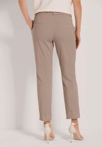 Beige op maat gemaakte broeken met een slim fit, voorzien van twee achterzakken, strakke lijnen en een enkellange zoom, gecombineerd met lichtgekleurde hakken.