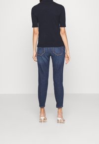 Námořnický top s krátkým rukávem v kombinaci s tmavě modrými slim džíny, které mají zadní kapsy a mírně se zužují směrem k kotníkům, nošeno s bílými podpatky.