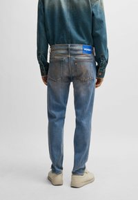 Light blue denim jeans with a straight fit, faded texture, and visible stitching, featuring a blue HUGO tag on the back waistband.