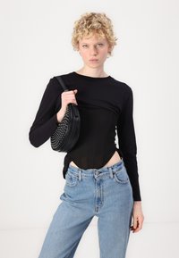 Zwarte lange mouwen top met een transparante bodice, hoge lichtblauwe jeans en een ronde zwarte tas met studs.