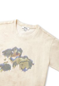 Camiseta color crema con una textura sutil, que presenta un diseño floral bordado multicolor en azul, verde y marrón. Etiqueta visible en el cuello.