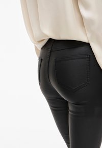Svart faux läderbyxor med en åtsittande design, som har två bakfickor och en jämn textur. Tyget har en lätt glansig finish.