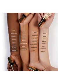 Fundamentalschatten auf Armen in verschiedenen Hauttönen ausgestellt, beschriftet mit Namen wie Chai, Honig und Vanille, um eine vielfältige Palette von Hautfarben zu präsentieren.