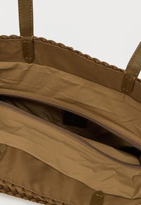 Καφέ τσάντα ώμου με υφαντό σχέδιο, διαθέτει τσέπη με φερμουάρ και λείο εσωτερικό. Ιδιαίτερες υφασμάτινες λαβές και άνοιγμα σε στυλ πουγκί.