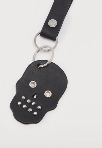 Μπρελόκ από μαύρο δέρμα σε σχήμα κρανίου, με ασημένιες μεταλλικές λεπτομέρειες για τα μάτια και το στόμα, με λεία υφή και στρογγυλεμένες άκρες.