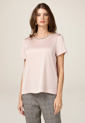 Helles rosa Satin-Oberteil mit kurzen Ärmeln und rundem Ausschnitt, verziert mit klaren Edelsteinen, kombiniert mit gemusterten grauen Hosen. Glatte Textur, lockere Passform.