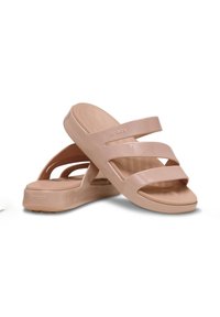 Pink slip-on sandals with three wide straps, smooth glossy surface, chunky sole, and "Crocs" logo on the side. Lightweight and minimalist design.