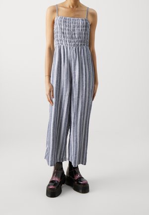 Blue and white striped jumpsuit with a fitted smocked bodice, thin shoulder straps, and wide-leg trousers, paired with black platform boots.