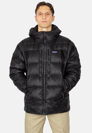 Geacă puffer neagră cu glugă, având un design matlasat, fermoar pe față, două buzunare pentru mâini și un mic logo pe piept.