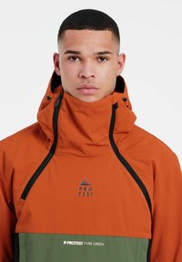 Orange- und grüne Jacke mit hohem Kragen, Reißverschluss vorne und Logo. Glattes, wasserabweisendes Material mit kontrastierenden Verzierungen.
