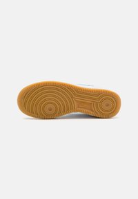 Nike sneaker sole with a round, textured pattern, featuring a gum rubber finish and surface grooves for traction. Blue accents visible on the sides.