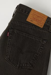 Πίσω τσέπη μαύρου τζιν Levi's 501 που δείχνει την καφέ δερμάτινη ετικέτα Levi Strauss και την κόκκινη υφασμάτινη ετικέτα Levi's.