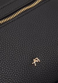 Czarna teksturowana skóra z wyraźnym złotym zamkiem błyskawicznym i małym złotym logo. Powierzchnia ma ziarnistą strukturę.