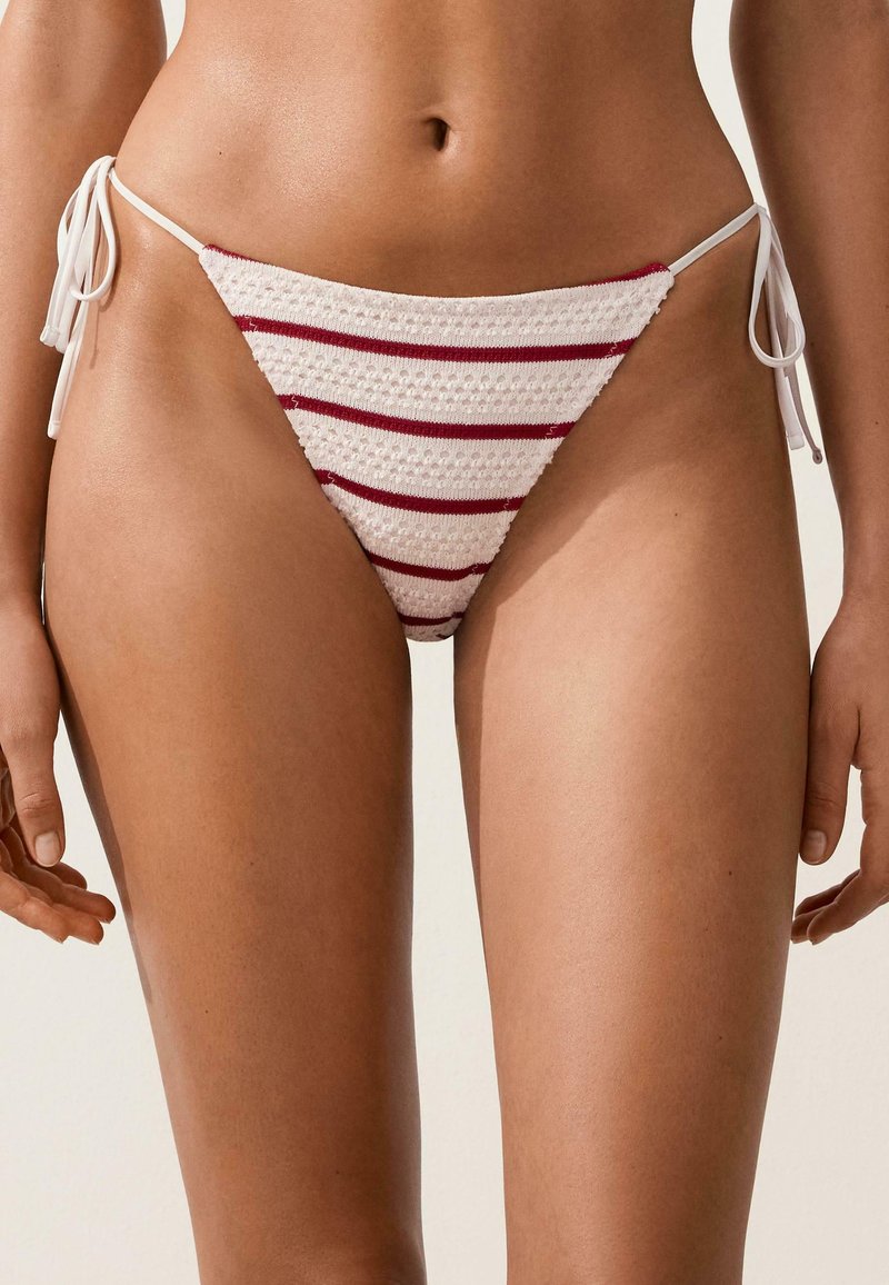 Gros plan d'une personne portant un bas de bikini blanc avec des rayures rouges horizontales et des liens sur les côtés.