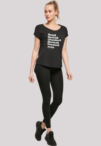 Svart T-skjorte med hvit tekst som lister opp navn; korte ermer; kombinert med svarte leggings og svarte treningssko. Minimalistisk design.