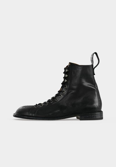 Botte montante en cuir noir avec fermeture à lacets à l'avant, détails brogue sur le bout, languette au talon et petit talon empilé.
