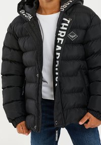 Chaleco inflable negro con capucha, que cuenta con costuras horizontales, un logotipo en la cremallera y un forro interior con texto en contraste.