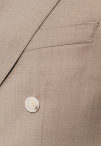 Μπεζ σακάκι με ανάγλυφο κολάρο, κλείσιμο με έναν λευκό κουμπί και θήκη στην θήκη με λεπτή υφή.