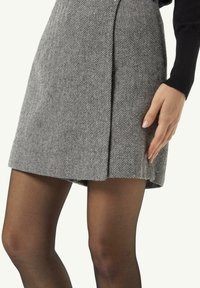 A grey houndstooth skirt with a pleated design, featuring a textured fabric and a straight cut, shown with a hand resting on it.