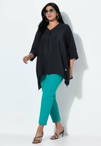 Tunica nera, larga e svasata con scollatura a V e spacco laterale, abbinata a pantaloni slim turchesi. Tacchi alti neri con laccetti completano l'outfit. Indossati occhiali da sole grandi.
