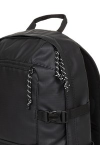 Zaino nero realizzato con materiali resistenti, caratterizzato da una texture liscia, coulisse nere e bianche a contrasto e chiusura laterale con fibbia.