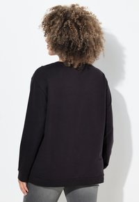 Felpa nera con maniche lunghe, vestibilità rilassata, polsini e orlo a coste, texture morbida e minimal dettagli sulle cuciture delle spalle.