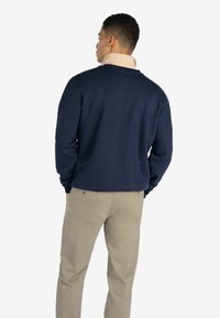 Suéter azul marino con cuello redondo, hecho de material suave, combinado con pantalones color arena que tienen bolsillos traseros y dos botones visibles.