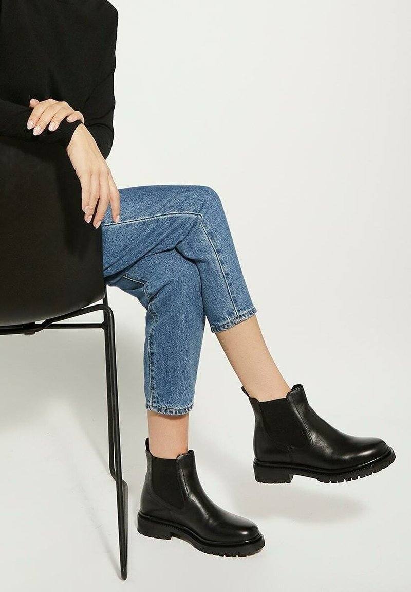 Bottes de cheville en cuir noir avec panneaux élastiques sur les côtés et semelles robustes en caoutchouc, associées à un jean en denim bleu raccourci. Design simple et épuré.