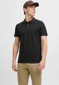 Zwart polo-shirt met korte mouwen en kraag, met drie knopen, een subtiele logo op de borst en gecombineerd met tan casual broeken.