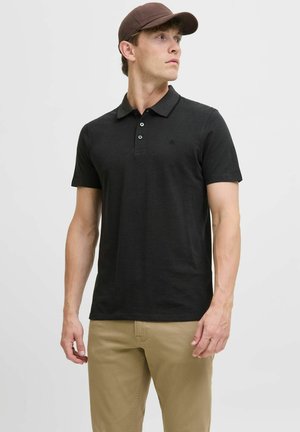 Zwart polo-shirt met korte mouwen en kraag, met drie knopen, een subtiele logo op de borst en gecombineerd met tan casual broeken.