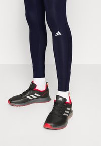 Svarta sportskor med röda detaljer, texturerade sulor och silverränder. Bärs med marinblå tights och vita strumpor.