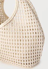 Μπεζ υφαντό τσάντα χειρός με στρογγυλεμένες λαβές και σφιχτό πλεκτό μοτίβο, που δείχνει λεπτομερή υφή και καμπυλωτό σχήμα.