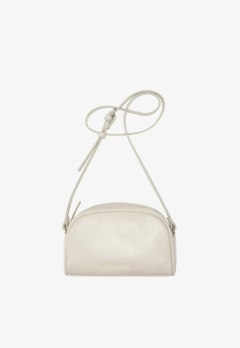 Pieni beige nahkainen olkalaukku pyöristetyllä yläosalla, säädettävällä hihnalla ja hillityllä etuosan logoyksityiskohdalla.