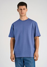 T-shirt blu a maniche corte realizzato in tessuto morbido, con una vestibilità comoda e collo rotondo. Abbinato a jeans in denim azzurri.