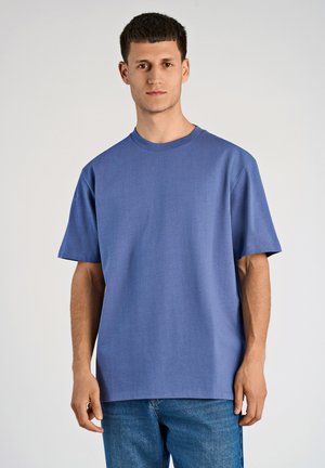 Niebieska koszulka z krótkim rękawem, wykonana z miękkiego materiału, charakteryzująca się luźnym krojem i okrągłym dekoltem. W zestawie z jasnoniebieskimi dżinsami.