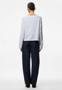 Light blue fuzzy sweater with a scalloped hem, paired with dark wide-leg jeans, viewed from the back.