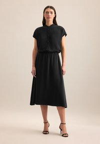 Schwarzes Midikleid mit kragenlosem Ausschnitt, kurzen Ärmeln und Knopfleiste. Verfügt über einen elastischen Taillenbund und eine glatte Textur.