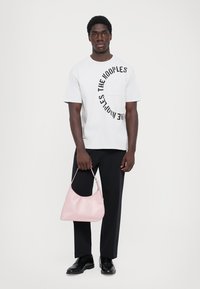 Tricou alb din bumbac cu text imprimat negru, pantaloni negri și o geantă de umăr roz moale. Textură netedă și design simplu.