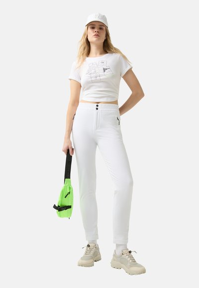 White cropped t-shirt featuring a graphic print, paired with white slim-fit joggers with black hardware and side pockets. Bright green crossbody bag.