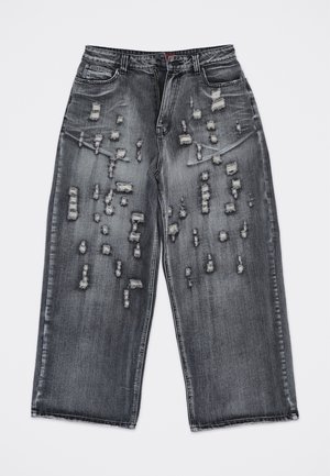 Vaqueros negros de pierna ancha con múltiples roturas horizontales y parches desgastados en la parte frontal de los muslos y las rodillas.