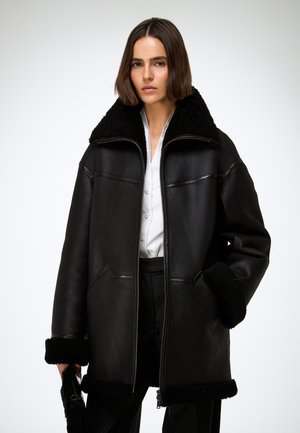 Giacca in pelle nera con colletto e polsini in shearling, dotata di cerniera frontale, due tasche e design ampio e oversize.