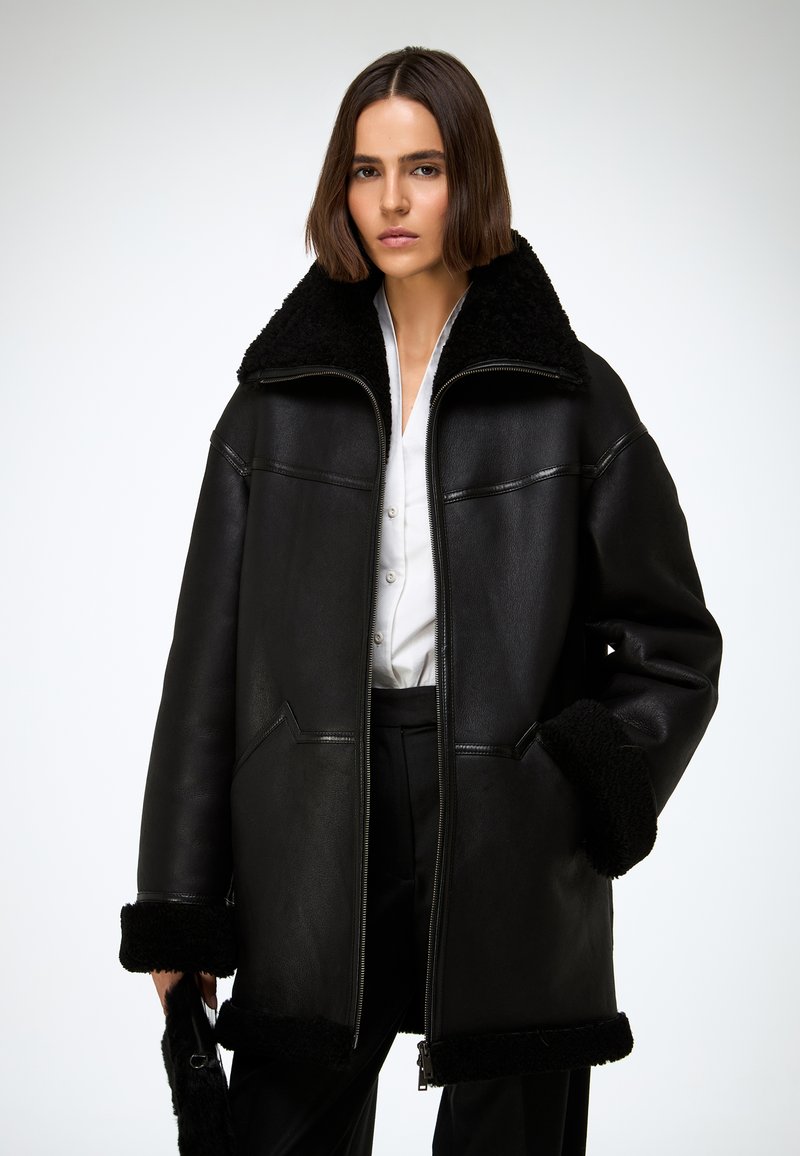 Veste en cuir noir avec col et poignets en peau lainée, dotée d'une fermeture éclair à l'avant, de deux poches, et d'une coupe ample et oversize.