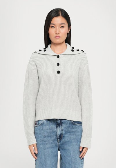Hellgrau gestrickter Pullover mit weitem Kragen, ausgestattet mit schwarzen dekorativen Knöpfen entlang der Schultern sowie gerippten Bündchen und Saum.